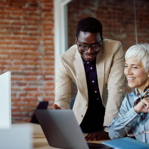 Happy African American businessman and his mature colleague using laptop while working in the office.