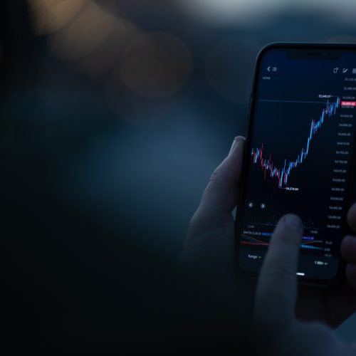 Investor checking stock exchange market data in mobile app on smartphone Investing online. Male hand monitoring stock exchange data on smartphone, using investment app for analyzing price activity in real time. Selective focus on mobile phone with financial chart on screen