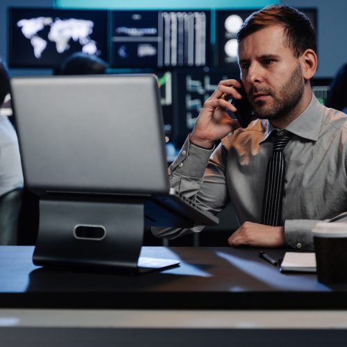 Successful trader businessman on a phone call investing in stock market using computer screens in busy modern office Successful trader businessman on a phone call investing in stock market using computer screens in busy modern office