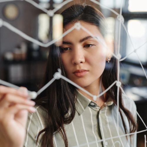Asian brokerage specialist drawing stock trading stats graph on glass wall in modern loft office