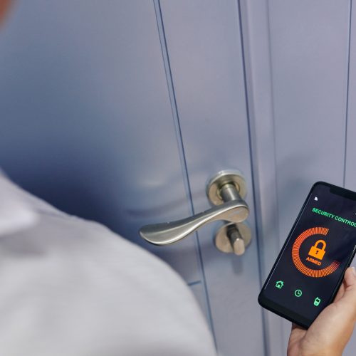 Woman using security control application on smartphone when leaving house and closing door