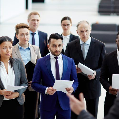 Group of young and mature intercultural politicians with papers listening to political leader at conference