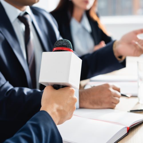 cropped view of journalist  with microphone interviewing politician during press conference on
