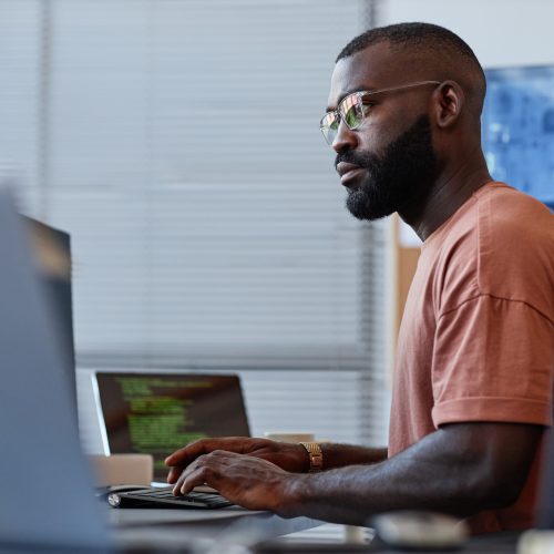 Side view portrait of black software developer using computer in high technology office, data systems and programming