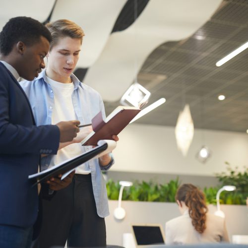 Young Business People in Corporate Company Low angle portrait of two young businessmen discussing work project while standing in modern office interior, copy space