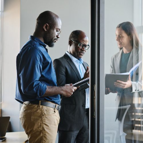 Young businessman preparing report while standing by his boss and female colleague showing document to director of company